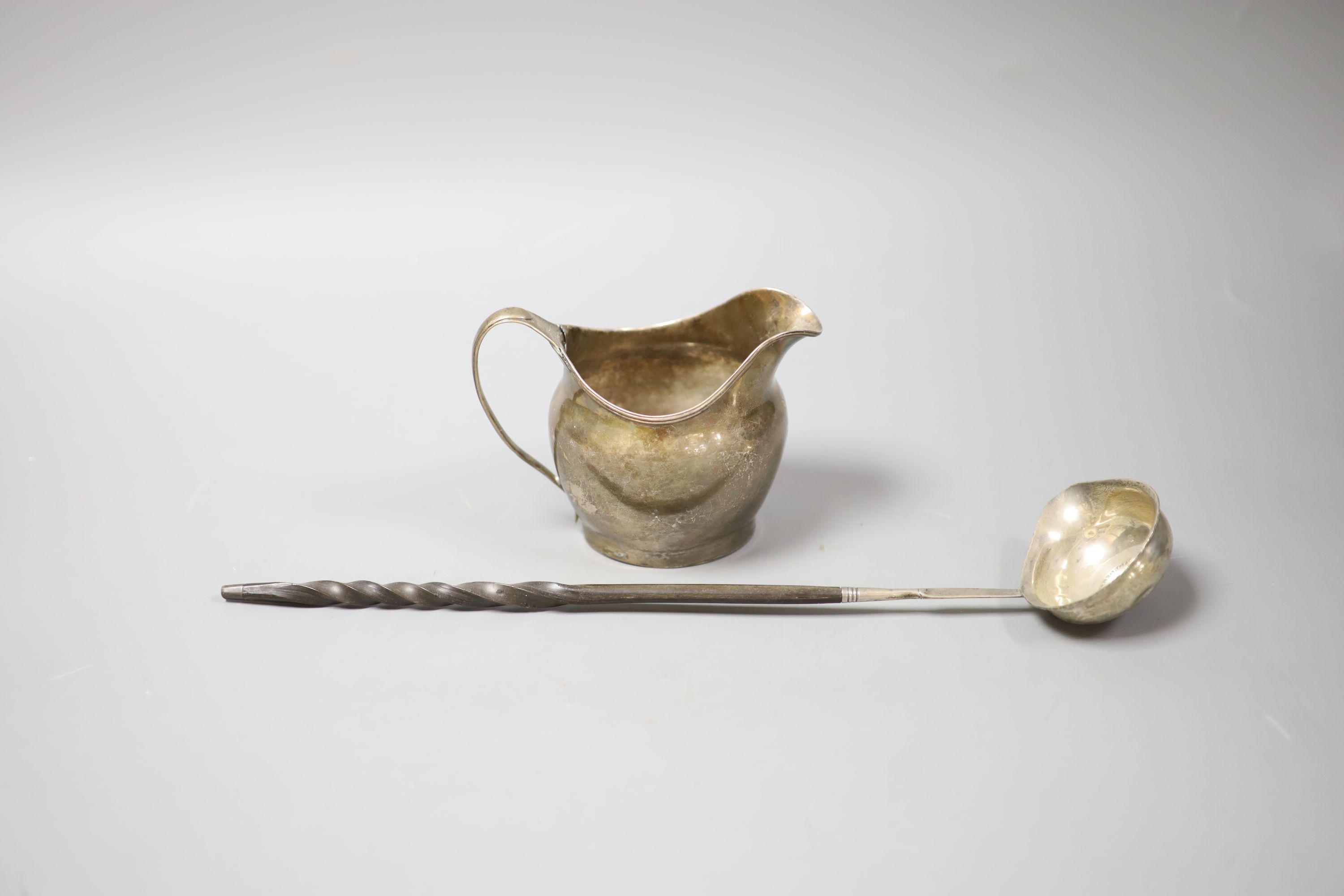 A George III silver cream jug, London, 1802 (a.f.)9.5cm and a 19th century white metal toddy ladle, 35cm.